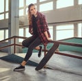 A beautiful young skateboarder girl wearing a checkered shirt sitting on a grind rail in skatepark indoors. Royalty Free Stock Photo