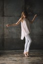 Beautiful young slender blond woman with curly hair in white trousers, a blouse and shoes in a loft studio is dancing. Soft Royalty Free Stock Photo