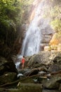 Beautiful young slim blonde woman with curly hair, wearing in red swimsuit is enjoy in lagoon of huge tropical waterfall Royalty Free Stock Photo