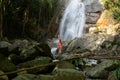 Beautiful young slim blonde woman with curly hair, wearing in red swimsuit is enjoy in lagoon of huge tropical waterfall Royalty Free Stock Photo