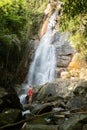 Beautiful young slim blonde woman with curly hair, wearing in red swimsuit is enjoy in lagoon of huge tropical waterfall Royalty Free Stock Photo