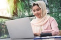 Beautiful young smiling asian muslim woman working on laptop sitting in living room at home. Royalty Free Stock Photo