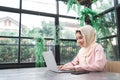 Beautiful young smiling asian muslim woman working on laptop sitting in living room at home. Royalty Free Stock Photo