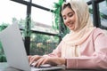 Beautiful young smiling asian muslim woman working on laptop sitting in living room at home. Royalty Free Stock Photo