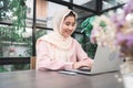 Beautiful young smiling asian muslim woman working on laptop sitting in living room at home. Royalty Free Stock Photo