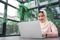 Beautiful young smiling asian muslim woman working on laptop sitting in living room at home. Royalty Free Stock Photo