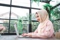 Beautiful young smiling asian muslim woman working on laptop sitting in living room at home. Royalty Free Stock Photo