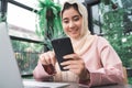 Beautiful young smiling asian muslim woman working on phone sitting in living room at home. Royalty Free Stock Photo