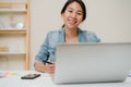 Beautiful young smiling asian woman working laptop on desk in living room at home. Asia business woman writing notebook document Royalty Free Stock Photo