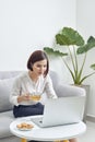 Beautiful young smiling asian woman working on laptop and drinking coffee in living room at home. Asia business woman working Royalty Free Stock Photo