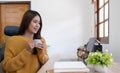 Beautiful young smiling asian woman working on laptop and drinking coffee in living room at home. Asia business woman working Royalty Free Stock Photo