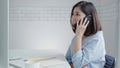 Beautiful young smiling asian woman working on laptop while sitting in a living room at home. Asian business woman using phone for Royalty Free Stock Photo