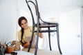 Young smiling brunette woman with braid carefully sanding old wooden chair Royalty Free Stock Photo