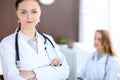 Beautiful young smiling female doctor standing in a hospital with her colleague in the background Royalty Free Stock Photo