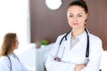 Beautiful young smiling female doctor standing in a hospital with her colleague in the background Royalty Free Stock Photo