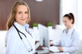 Beautiful young smiling female doctor standing in a hospital with her colleague in the background Royalty Free Stock Photo