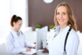 Beautiful young smiling female doctor standing in a hospital with her colleague in the background Royalty Free Stock Photo