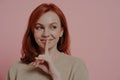 Beautiful young smiling ginger woman putting finger on lips and making hush sign Royalty Free Stock Photo
