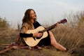 beautiful young smiling woman playing melody on acoustic guitar while sitting in field among tall dried grass. Royalty Free Stock Photo