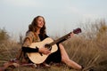 beautiful young smiling woman playing melody on acoustic guitar while sitting in field among tall dried grass. Royalty Free Stock Photo