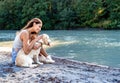 Beautiful young smiling woman sitting on sand hugging dog near the river enjoying the silence and beauty of nature. Royalty Free Stock Photo