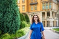 Beautiful young smiling woman walking in city park near famous old architecture building at summer day wearing dress and looking Royalty Free Stock Photo