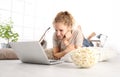 beautiful young smiling woman watch a movie at the computer eating popcorn lying on living room wooden floor in comfortable home Royalty Free Stock Photo