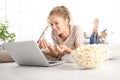 beautiful young smiling woman watch a movie at the computer eating popcorn lying on living room wooden floor in comfortable home Royalty Free Stock Photo