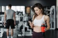 Beautiful young sportswoman in sportswear and earphones is holding a bottle of water, listening to music using a phone and smiling Royalty Free Stock Photo