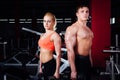 Beautiful young sporty couple showing muscle and posing with dumbbells in gym during photoshooting