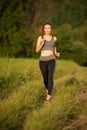 Beautiful young sporty woman workout in nature runs on a path on meadow