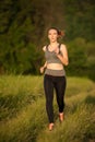 Beautiful young sporty woman workout in nature runs on a path on meadow