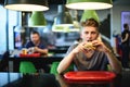 Beautiful young student eats a burger in a fast food restaurant. Tasty and harmful food. Nooning.