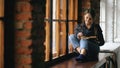 Beautiful young student girl reading book sit on windowsill in university classroom indoors Royalty Free Stock Photo