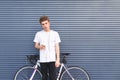 Beautiful young student standing with a smartphone in his hands and headphones near a bicycle on the background