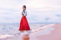 Beautiful young stylish boho woman walking on the beach at sunset