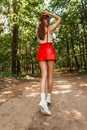 Beautiful young stylish woman with a slender body and sexy legs in fashionable summer clothes with a red skirt and white shoes Royalty Free Stock Photo