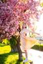 Beautiful young stylish woman walking in sakura park and enjoy beauty of pink flowers. Blooming sakura cherry tries in