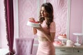 Beautiful young tall girl in a pink dress holding a cake and smiling. Pink interior style Royalty Free Stock Photo