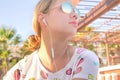 A beautiful young tanned girl listening music with earphones in sunglasses under palms shadow