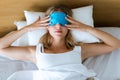 Beautiful young tired woman trying to sleep with sleep mask resting on bed in bedroom at home. Royalty Free Stock Photo