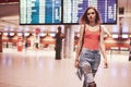 Beautiful young tourist girl with backpack in international airport, near flight information board Royalty Free Stock Photo