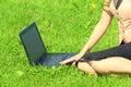 A beautiful young white girl in a pink jacket and black skirt and with long hair sitting on green grass, on the lawn and working Royalty Free Stock Photo