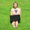 A beautiful young white girl in a pink jacket and black skirt and with long hair sitting on green grass, on the lawn and working Royalty Free Stock Photo