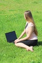 A beautiful young white girl in a pink jacket and black skirt and with long hair sitting on green grass, on the lawn and working Royalty Free Stock Photo