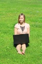 A beautiful young white girl in a pink jacket and black skirt and with long hair sitting on green grass, on the lawn and working Royalty Free Stock Photo