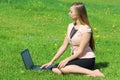 A beautiful young white girl in a pink jacket and black skirt and with long hair sitting on green grass, on the lawn and working Royalty Free Stock Photo