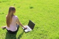 A beautiful young white girl in a pink jacket and black skirt and with long hair sitting on green grass, on the lawn and working Royalty Free Stock Photo