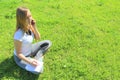 A beautiful young white girl in a white t-shirt and with long hair sitting on green grass, on the lawn, talking on a cell phone Royalty Free Stock Photo