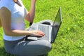 A beautiful young white girl in a white t-shirt and with long hair sitting on green grass, on the lawn and working behind a black Royalty Free Stock Photo